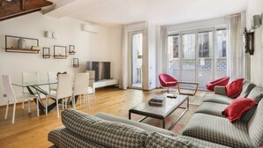 Un salon moderne avec une table à manger en verre, des chaises blanches, un ensemble de canapés et un fauteuil rouge.