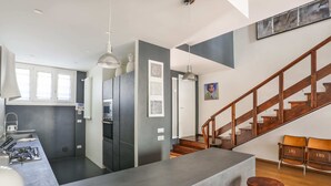 Une cuisine moderne dotée d’un îlot central, d’un coin repas avec des tabourets de bar et d’un escalier avec des rampes en bois.
