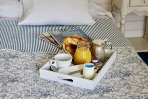 A breakfast tray with a cup, a glass of orange juice, a bottle of milk, and a jar of jam on a bed with a striped bedspread and a magazine. - Hôtel Sainte Marie (Lourdes)