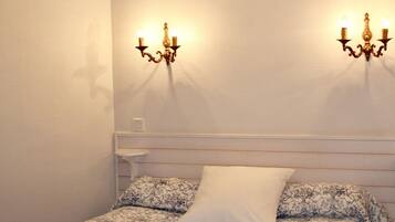 A bedroom with a bed, two wall-mounted sconces, a nightstand, and a plain wall.