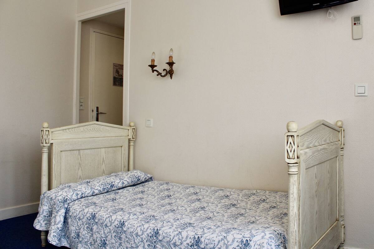 A bedroom with a single bed, a TV mounted on the wall, and a door leading to another room.
