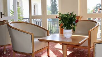 Une pièce comprenant une table et deux chaises, une plante en pot posée sur la table, et donnant sur un balcon avec une balustrade.