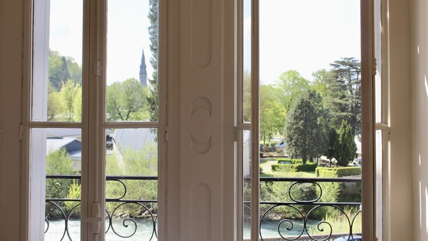 A view through a window with a balcony railing, a river, and trees in the background. - Hôtel Sainte Marie (Lourdes)