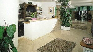 A spacious living area with a kitchen, a large central plant, and a dining area with a high ceiling and natural light. - Hotel Parco dei Principi (Grottammare)