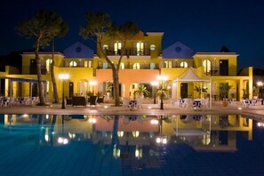 Un hotel con piscina, mobiliario exterior y una fachada bien iluminada.
