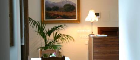 A dining area with a table, chairs, a potted plant, a painting on the wall, and a lamp.