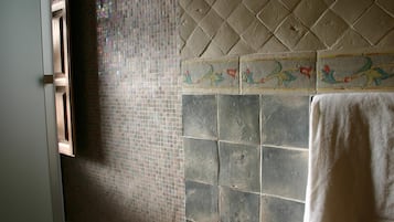 Un baño con paredes de mosaico, una zona de ducha con azulejos y una toalla colgada en la pared.