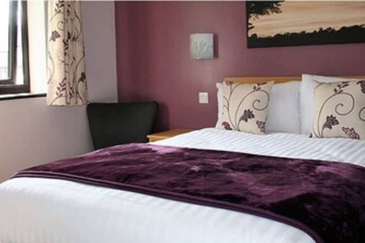 A bedroom with a bed, a window with curtains, a chair, and a painting on the wall.