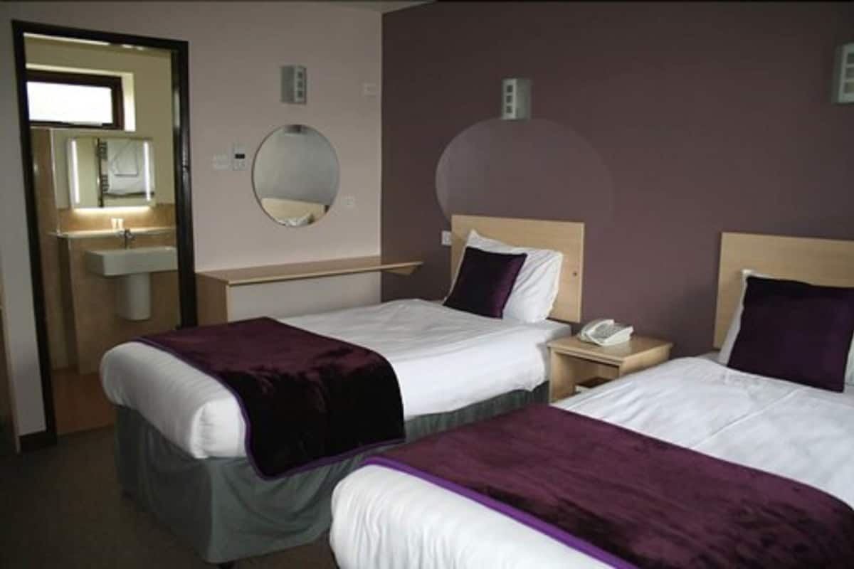 A hotel room with two beds, a round mirror, a small round table, and a bathroom visible through an open door.