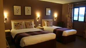 Une chambre d’hôtel avec deux lits, chacun doté d’une tête de lit et de tables de chevet. Les murs sont ornés de lampes murales et de tableaux encadrés.