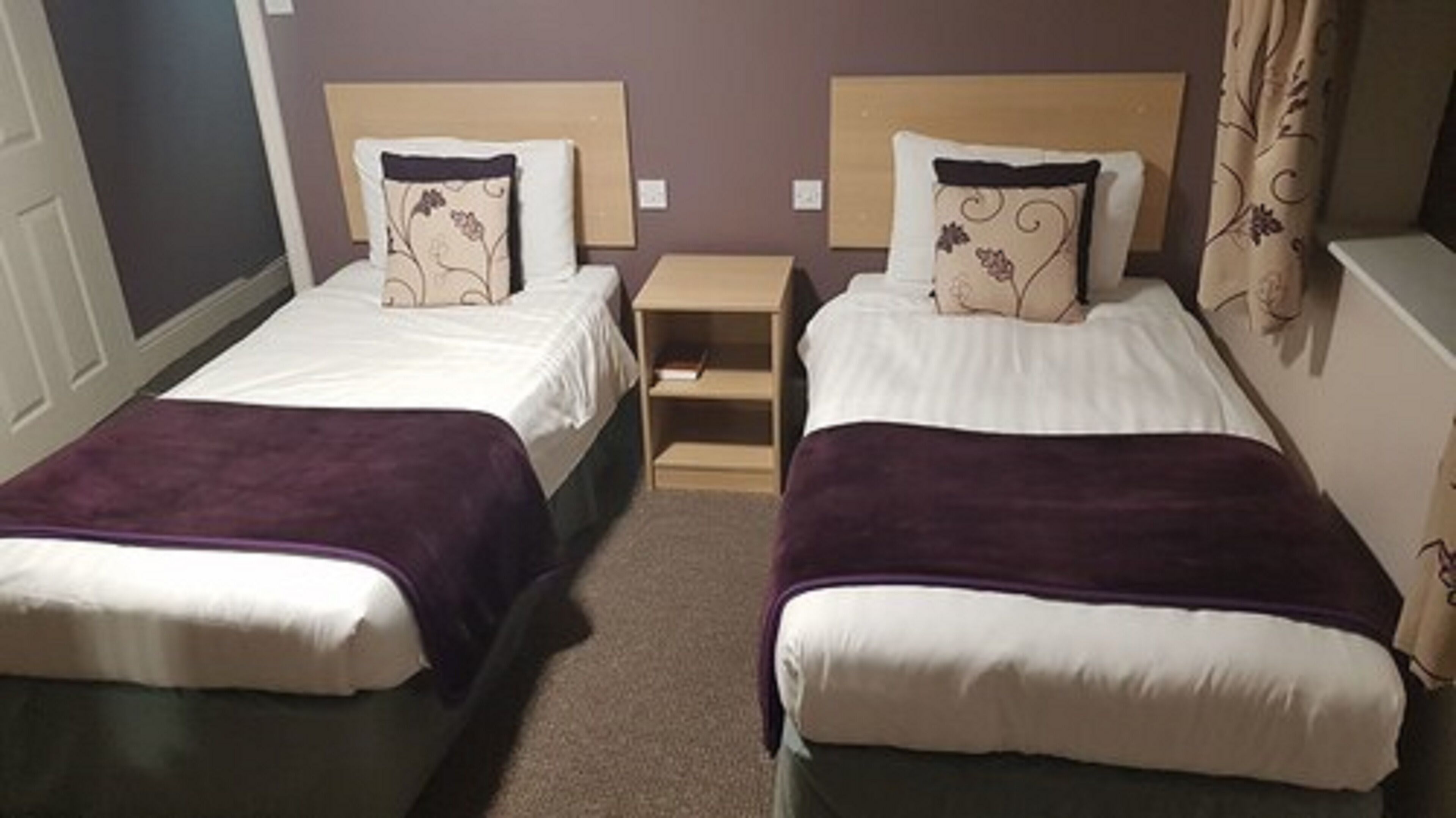 Een hotelkamer met twee eenpersoonsbedden, elk met hoofdeinde, nachtkastje en een klein tafeltje.