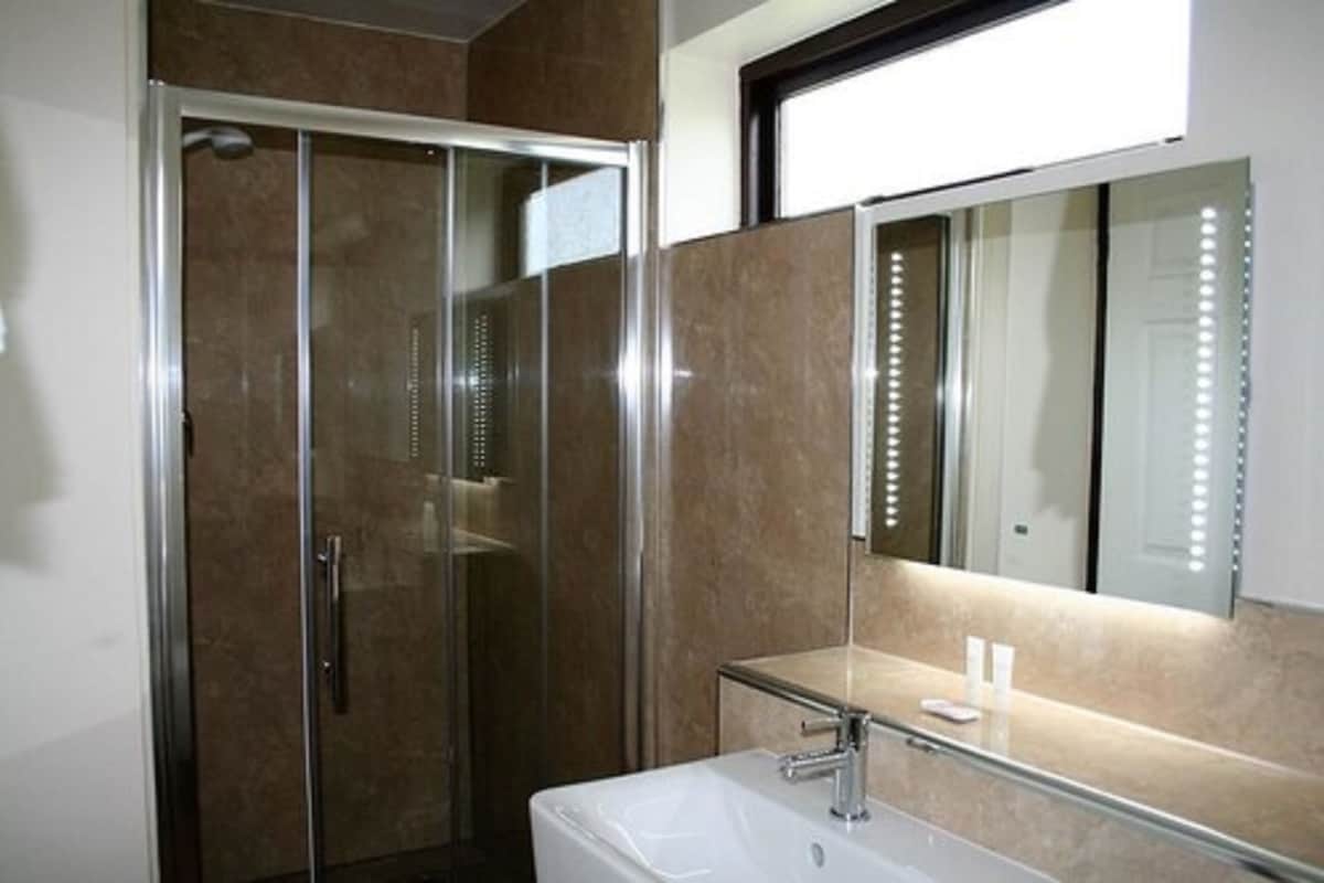 Une salle de bain avec une douche à parois de verre, un lavabo avec un miroir et un mur éclairé.
