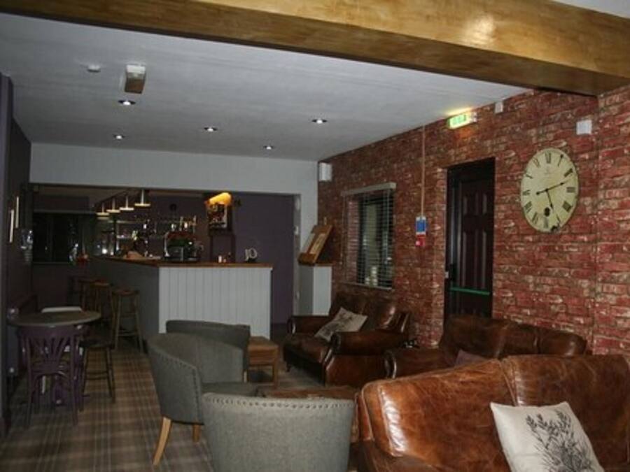 A cozy lounge area with leather sofas, a bar in the background, and a brick wall.