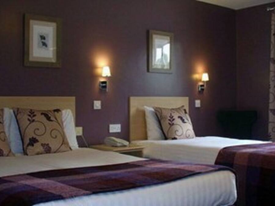 A hotel room with two beds, a window with curtains, and wall-mounted lamps.