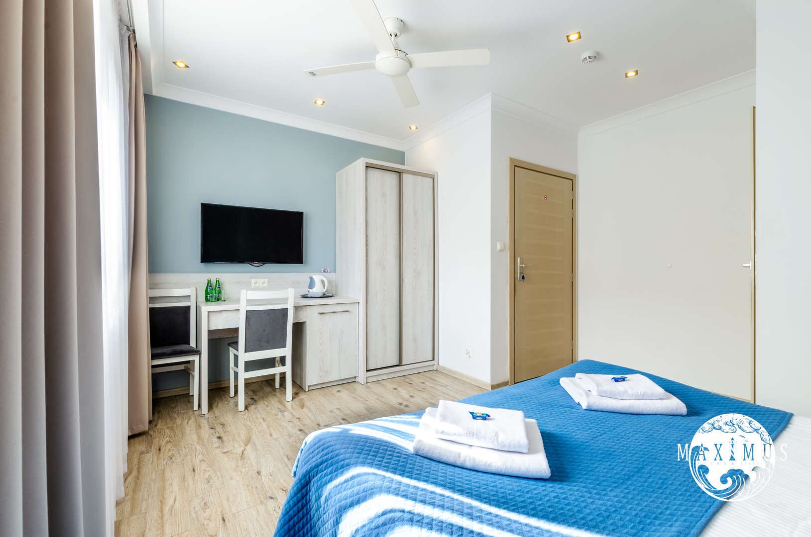 A hotel room with a bed, a desk with a chair, a television, and a wardrobe.