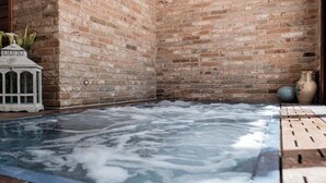 Uma área de spa com hidromassagem, cercada por paredes de tijolo, um armário decorativo branco e um vaso.