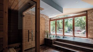 Interior moderno com sauna de madeira, porta de vidro e vista para o exterior.