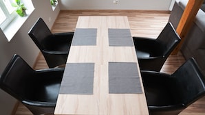 A dining area with a wooden table and black chairs, each with a grey placemat. - Apartamenty Marina (Ustka)