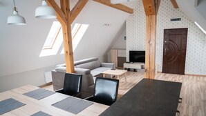 A modern loft-style room with a dining area, a sofa, a TV, and a wooden ceiling structure. - Apartamenty Marina (Ustka)
