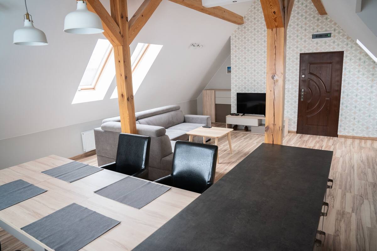 Ett modernt rum i loftstil med en matplats, en soffa, en TV och en takkonstruktion i trä.