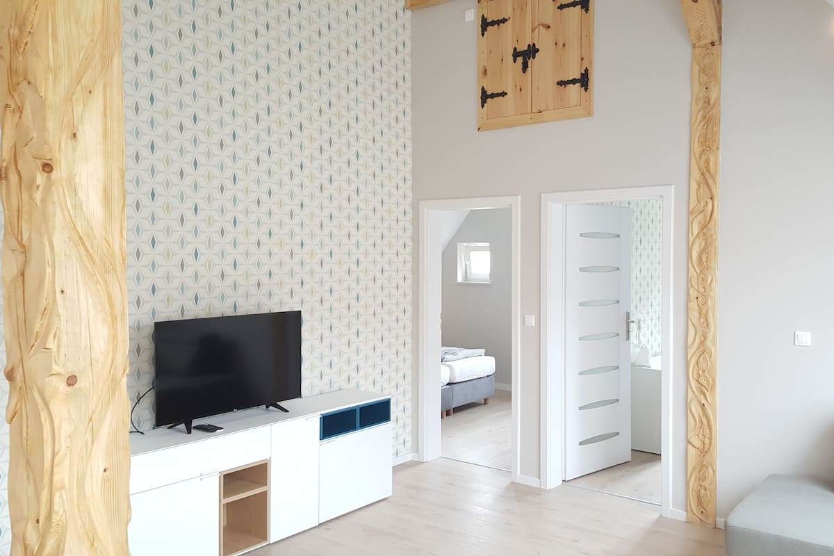 Ett modernt vardagsrum med en platt-TV placerad på ett vitt skåp, en grå soffa och en väggpanel i trä som ger rummet en accentfärg.