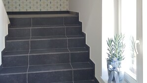 A staircase with dark tiles leading to a landing, a patterned wall, and a window with a potted plant. - Apartamenty Marina (Ustka)