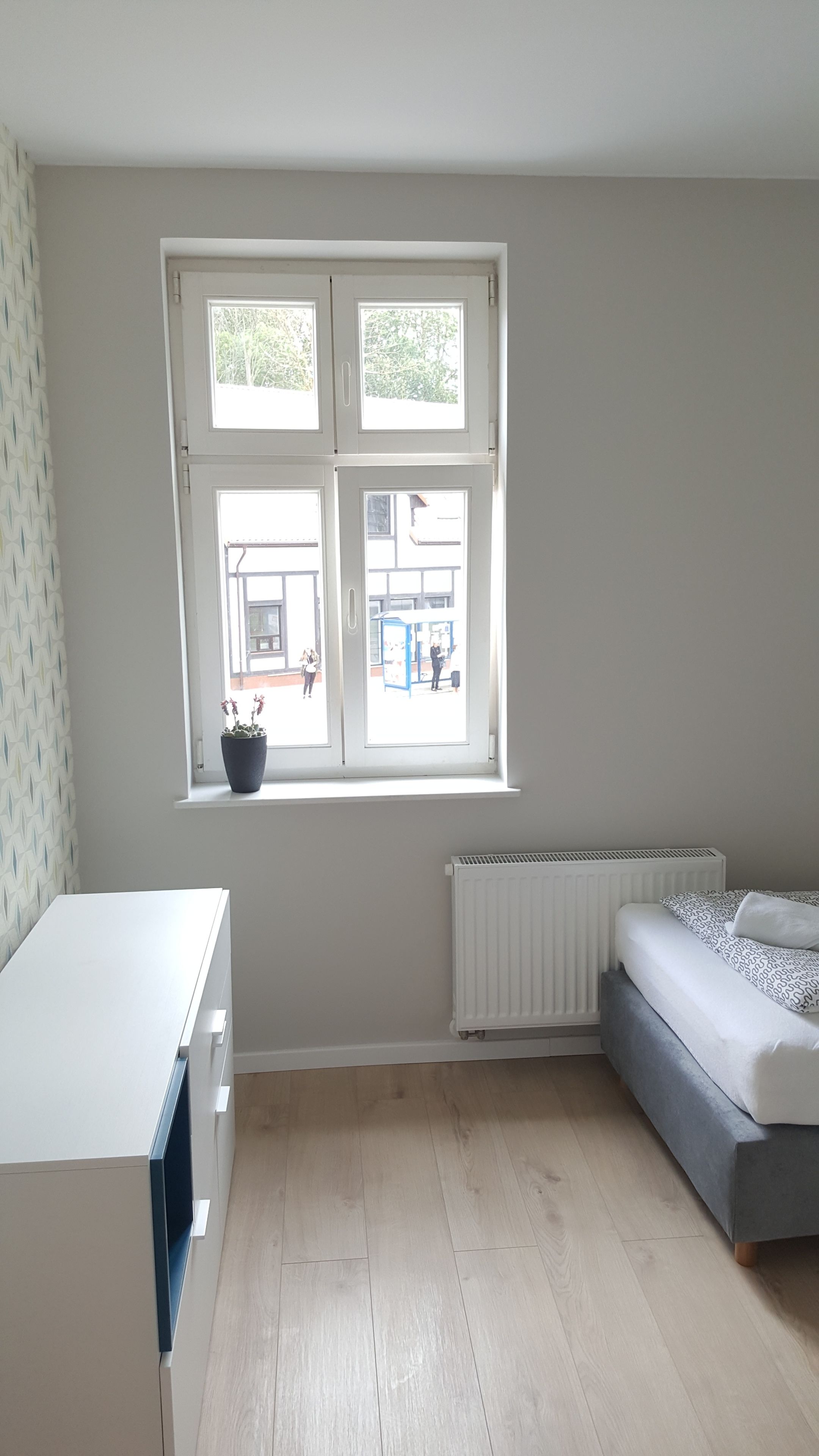 A room with a large window, a radiator, a bed, and a desk.