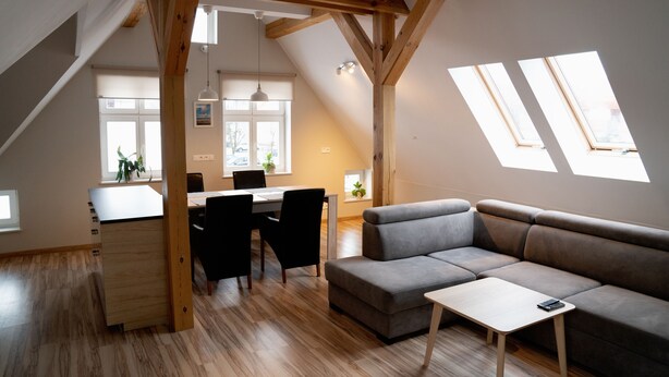 A modern loft apartment with a dining area, a gray sofa, and skylights. - Apartamenty Marina (Ustka)