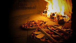Two pizzas baking in a wood-fired oven with flames visible in the background. - Hotel Cima d'Asta (Pieve Tesino)