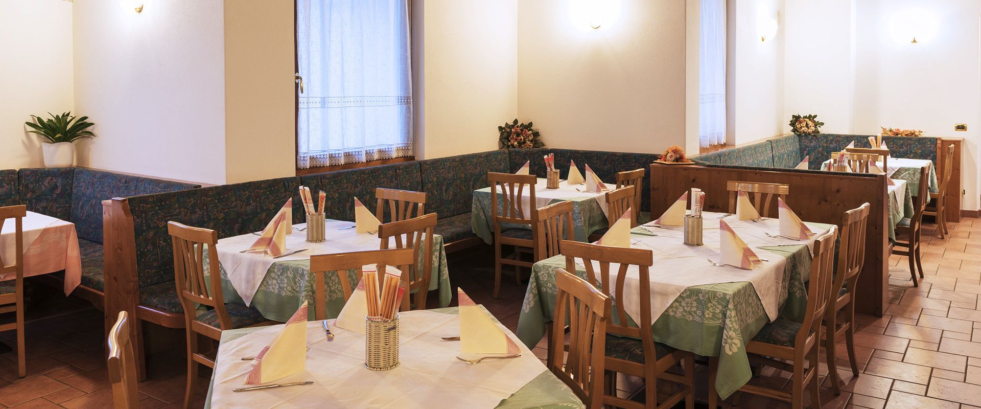 A restaurant with booths and tables, each with a tablecloth and napkin holder.