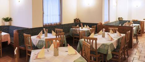 A restaurant with booths and tables, each with a tablecloth and napkin holder.