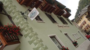 A building with a green facade, geometric patterns, wooden balconies, and flower boxes. - Hotel Cima d'Asta (Pieve Tesino)