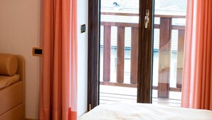 A hotel room with a bed, a sofa, and a sliding glass door leading to an outdoor balcony. - Hotel Cima d'Asta (Pieve Tesino)
