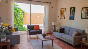 Un salon comprenant un canapé, des fauteuils, une table basse et donnant sur un jardin grâce à une porte coulissante.