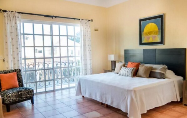 Une chambre d’hôtel avec un lit, une chaise, une fenêtre avec des rideaux et un tableau au mur.