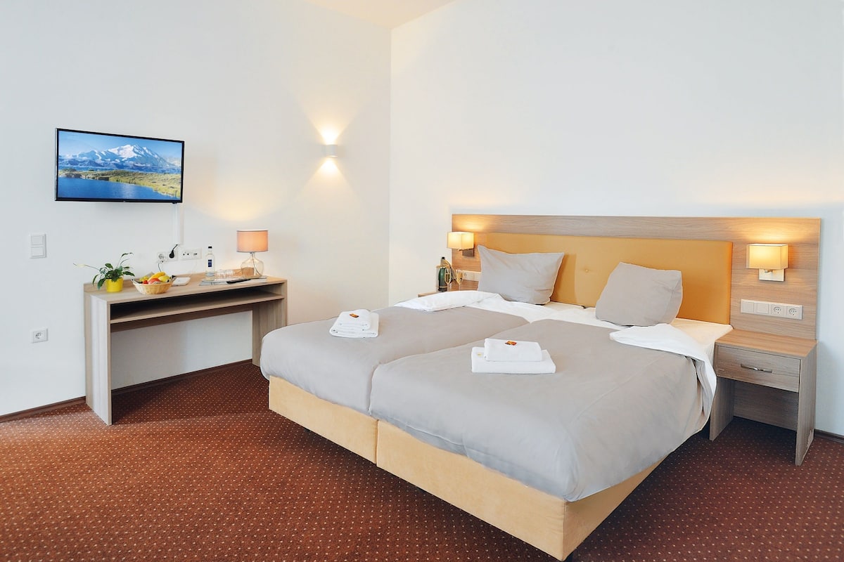 Ein Hotelzimmer mit einem großen Bett, einem Schreibtisch mit Computer und einem an der Wand montierten Fernseher.
