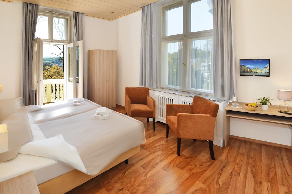 Ein Hotelzimmer mit Bett, Schreibtisch, Stuhl, Heizkörper und einem Fenster mit Aussicht.