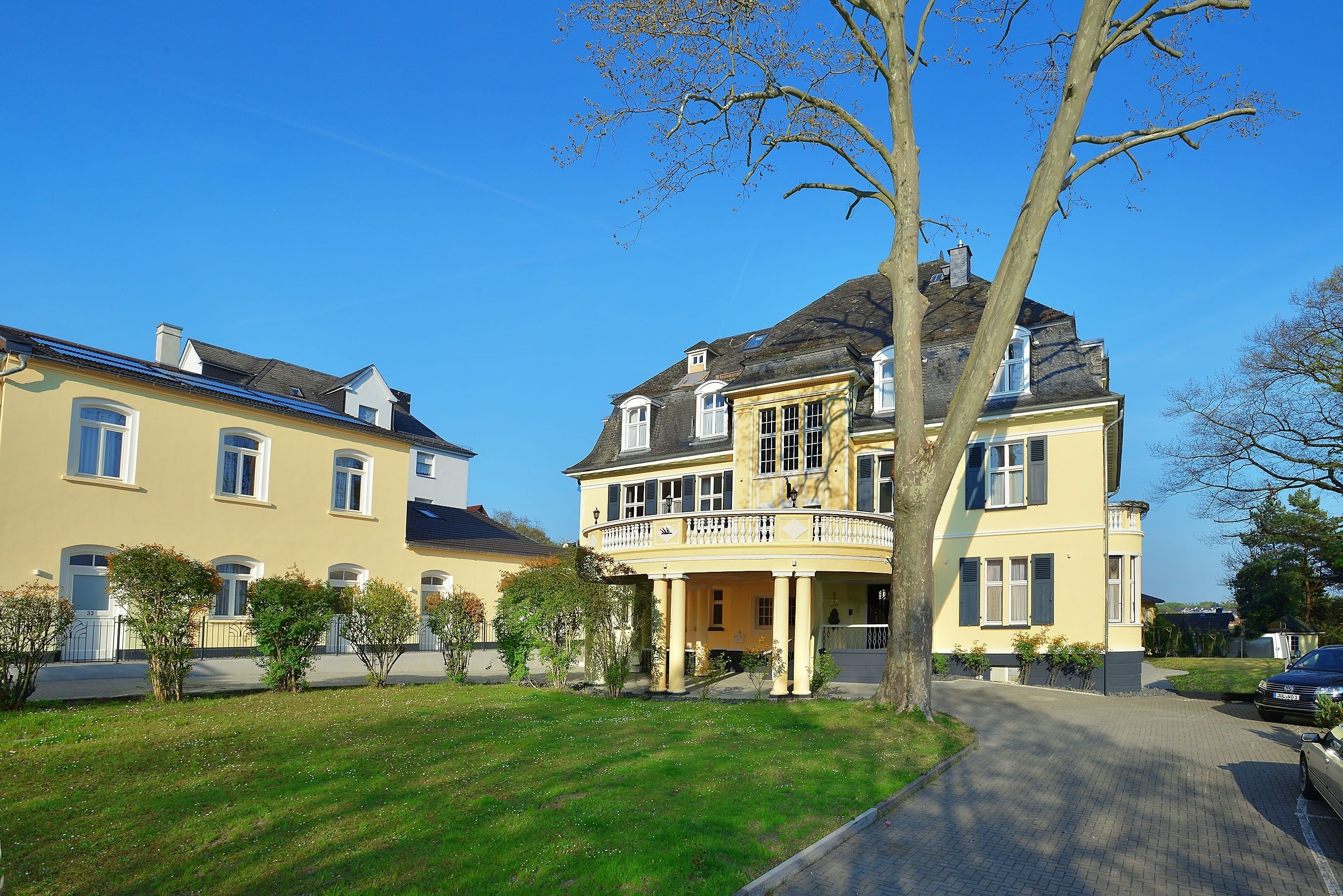 A large, yellow two-story house with a balcony, surrounded by a well-maintained lawn and trees.