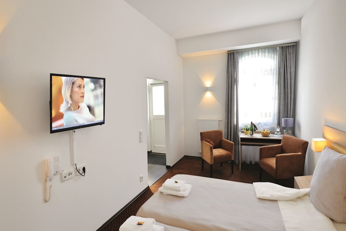 Ein Hotelzimmer mit Bett, Schreibtisch, zwei St ühlen, Fernseher und einem Fenster mit Vorhängen.