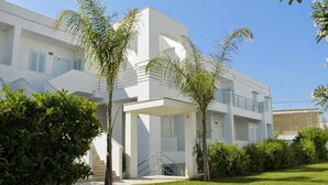 A modern building with a white facade, multiple balconies, and a covered entrance area. - Blumarine Residence Club (Ostuni)