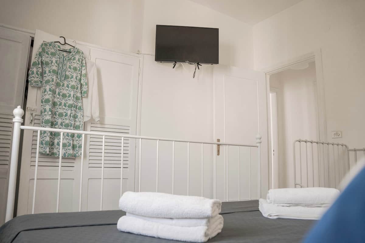 Un dormitorio con cama, radiador blanco, televisor montado en la pared y puerta blanca.