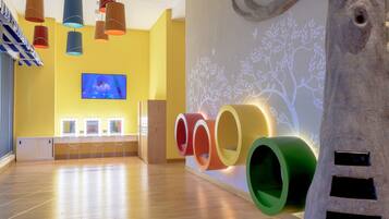 A spacious room with wooden flooring, colorful cylindrical structures, a mounted tree sculpture, and a television on the wall.