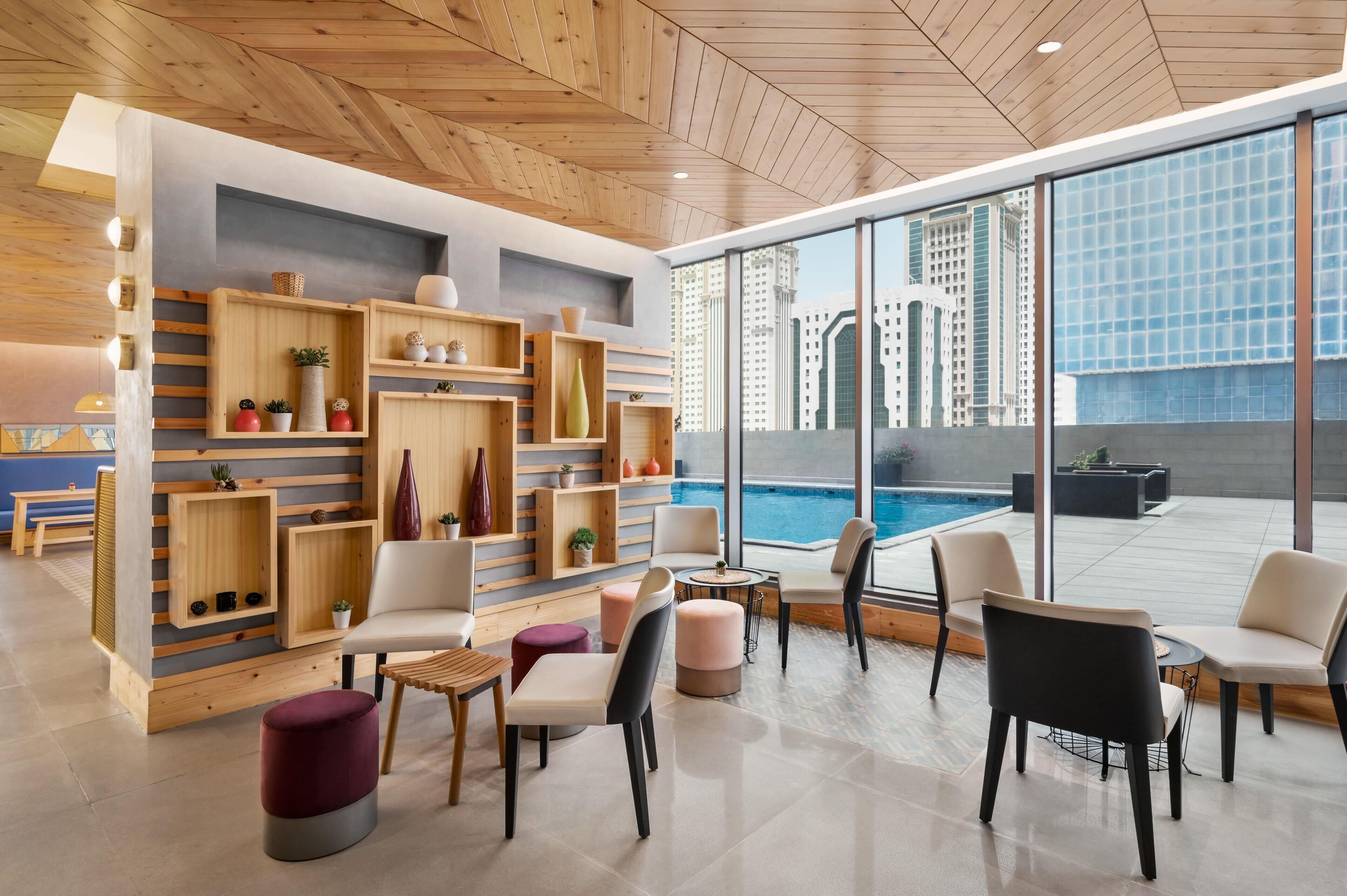 A modern lounge area with wooden shelving, comfortable seating, and a view of the city skyline.