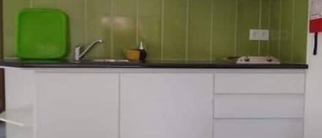 Cocina compacta con armarios blancos, salpicadero verde y una pequeña encimera.