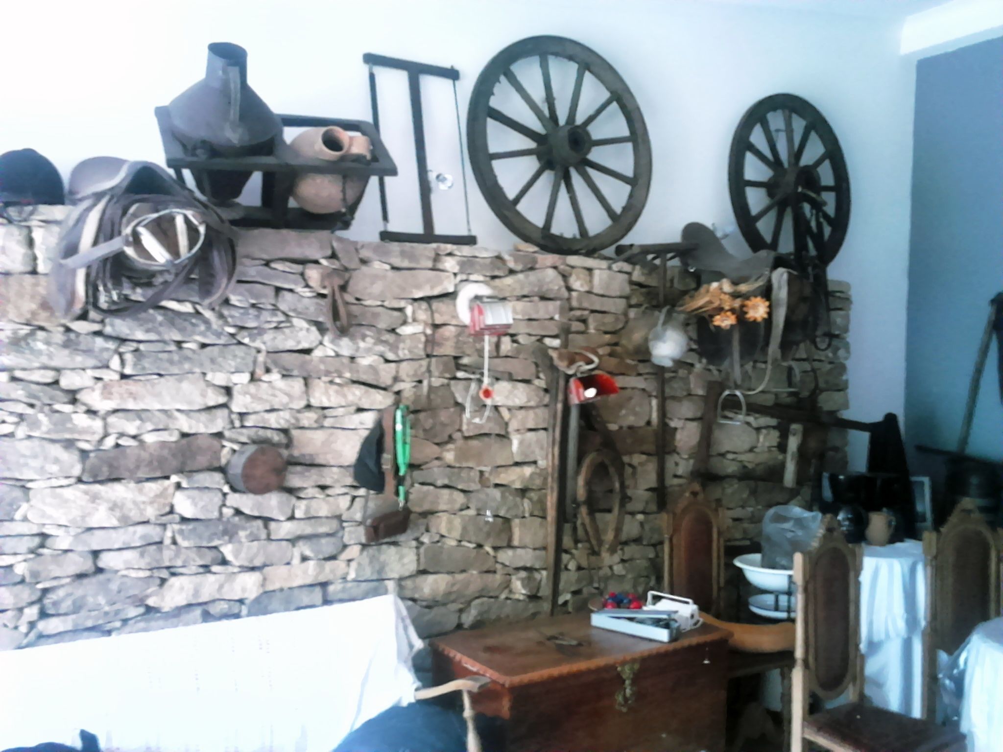 Una habitación rústica con pared de piedra, muebles de madera y diversos objetos utilitarios y decorativos.