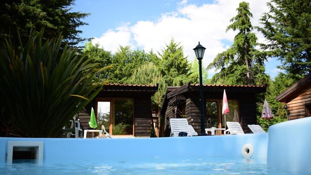 Zona de piscina con cabañas de madera, sillas de descanso y un farol.