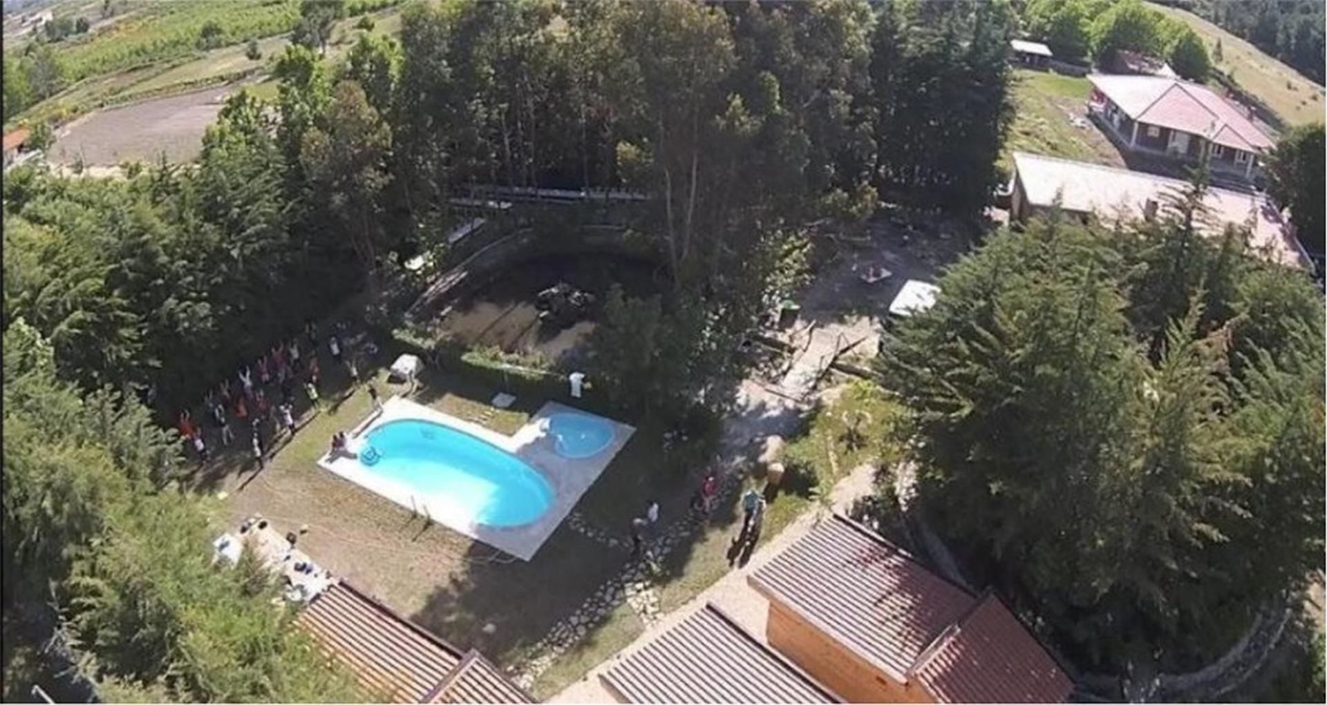 Luchtbeeld van een woongebied met een zwembad, omringd door bomen en een huis met een rood dak.