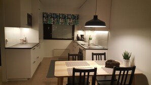 Cocina compacta con comedor, que incluye una mesa de madera, sillas, una lámpara colgante y una pequeña planta en maceta.