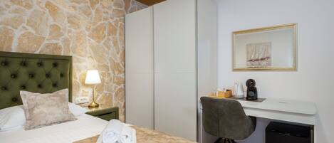 Habitación de hotel con cama, escritorio, silla, lámpara, calentador pequeño y cubo de basura.