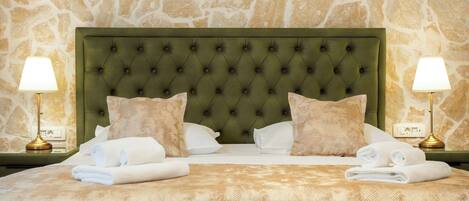 Uma cama bem arrumada com cabeceira verde, roupa de cama branca e duas luminárias de apoio.
